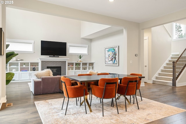 dining space with wood finished floors, recessed lighting, baseboards, a brick fireplace, and stairs