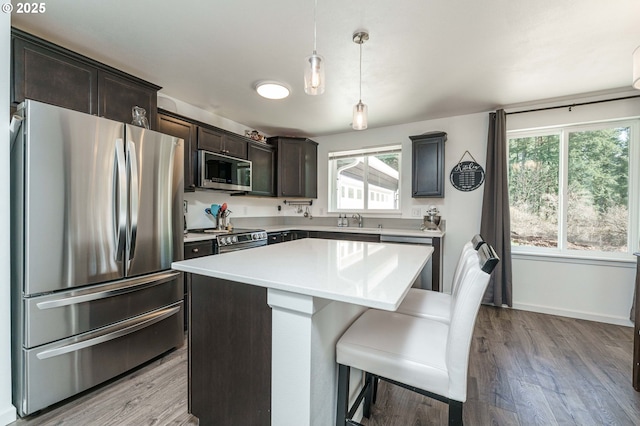 kitchen featuring a kitchen island, wood finished floors, stainless steel appliances, light countertops, and dark brown cabinets