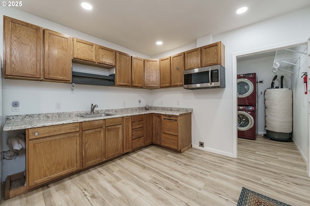 kitchen with stacked washing maching and dryer, a sink, light wood-style floors, stainless steel microwave, and brown cabinets