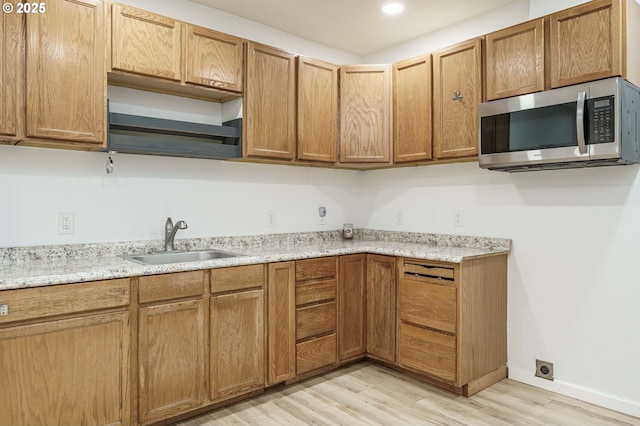 kitchen with light wood-type flooring, a sink, stainless steel microwave, brown cabinetry, and baseboards