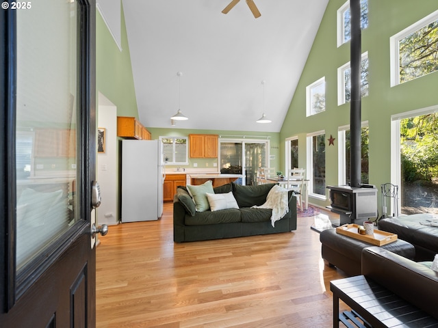 living room featuring a towering ceiling, a wood stove, ceiling fan, and light hardwood / wood-style flooring