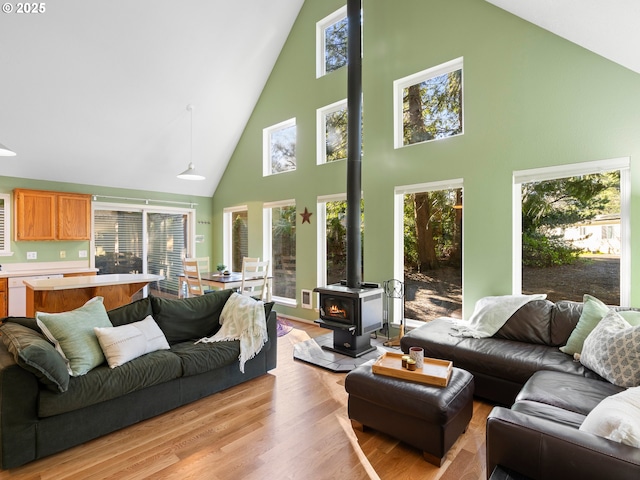 living room featuring lofted ceiling, plenty of natural light, a wood stove, and light wood-type flooring