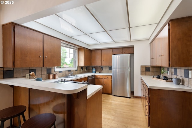 6807 SE Cesar E Chavez Blvd, Portland, OR 97202 - kitchen featuring appliances with stainless steel finishes, a peninsula, backsplash, light wood finished floors, and light countertops