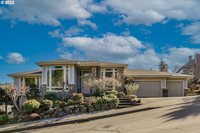 prairie-style home featuring a garage, driveway, stone siding, and stucco siding