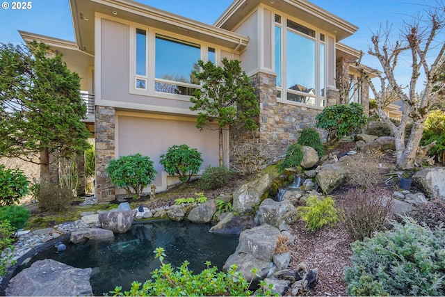 view of property exterior featuring stone siding, a small pond, and stucco siding