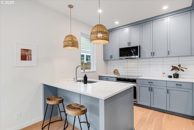 kitchen featuring sink, hanging light fixtures, light hardwood / wood-style flooring, tasteful backsplash, and stainless steel appliances