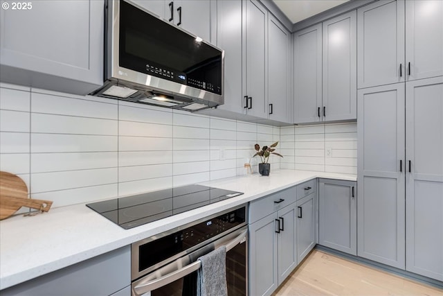 kitchen featuring light stone countertops, backsplash, stainless steel appliances, and gray cabinetry