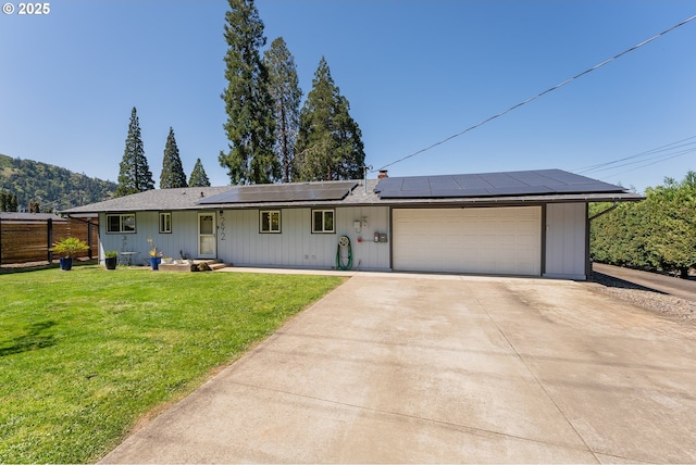ranch-style home with concrete driveway, fence, a front yard, a garage, and solar panels