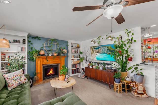 living room with a warm lit fireplace, carpet flooring, and a ceiling fan