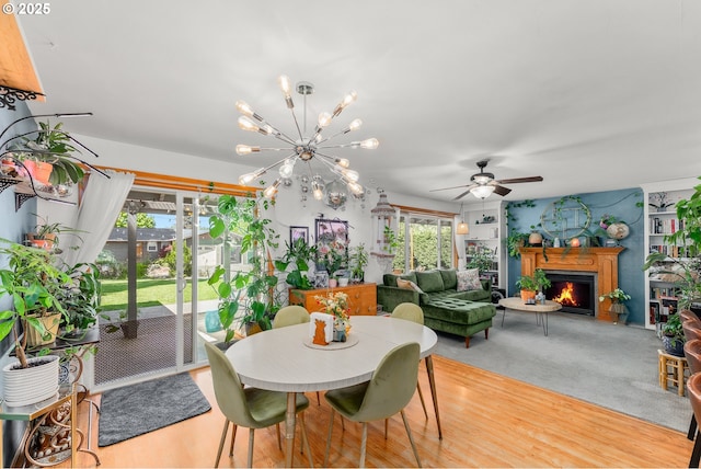 dining space featuring ceiling fan with notable chandelier and a warm lit fireplace