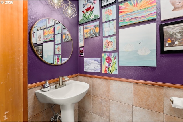 bathroom featuring wainscoting, a sink, and tile walls