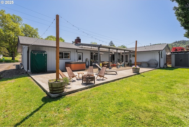 back of house with a chimney, a patio area, a hot tub, a yard, and an outdoor fire pit