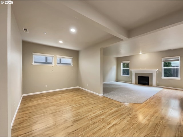 unfurnished living room featuring visible vents, baseboards, light wood-type flooring, beam ceiling, and plenty of natural light