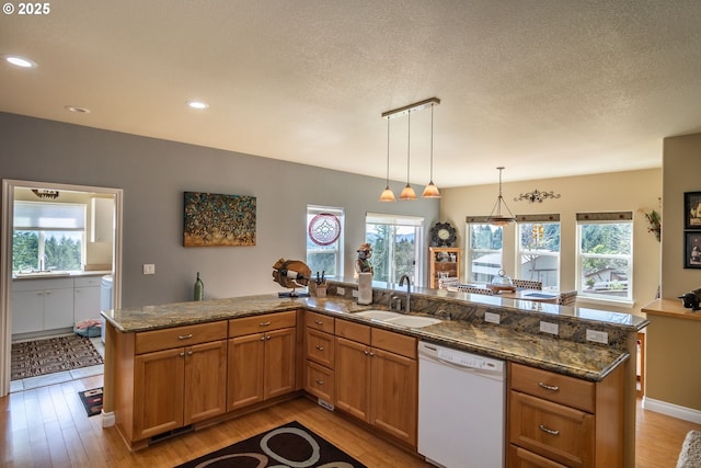kitchen featuring a sink, light wood-style floors, pendant lighting, white dishwasher, and brown cabinetry
