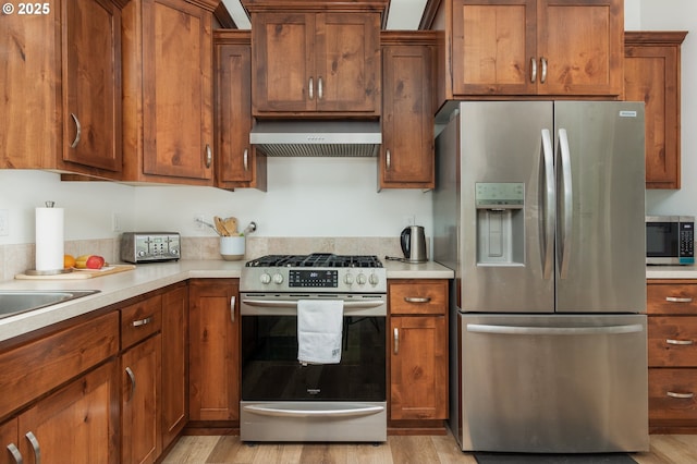 1937 NE 7th Dr, Lincoln City, OR 97367 - kitchen featuring appliances with stainless steel finishes, extractor fan, light countertops, light wood-style floors, and brown cabinetry