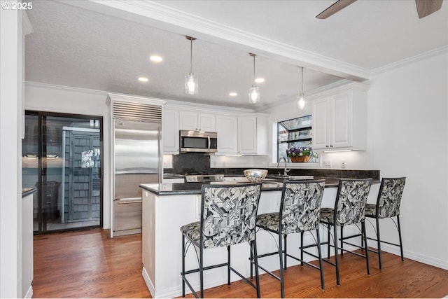 kitchen with dark countertops, a peninsula, a kitchen bar, appliances with stainless steel finishes, and white cabinetry