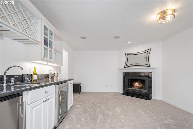 kitchen featuring a sink, dark stone countertops, light colored carpet, glass insert cabinets, and beverage cooler