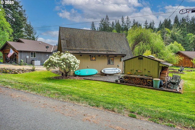 view of front of home with a front yard, an outbuilding, central AC unit, and a shingled roof