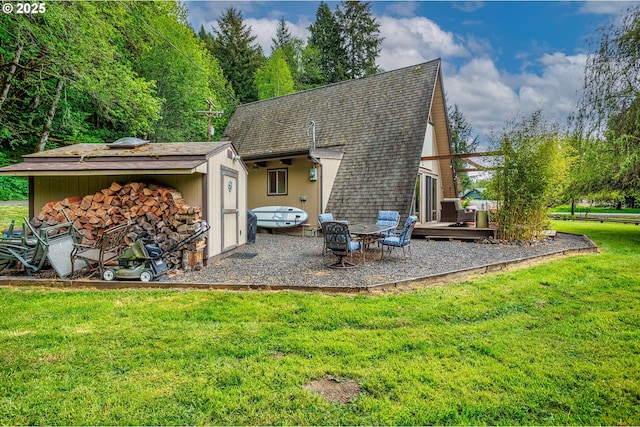 back of house featuring a lawn, a shingled roof, a storage shed, an outbuilding, and a patio