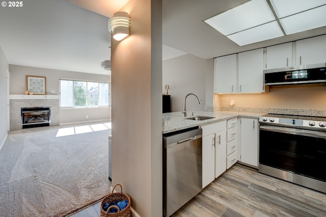 kitchen featuring white cabinetry, a tiled fireplace, appliances with stainless steel finishes, and a sink