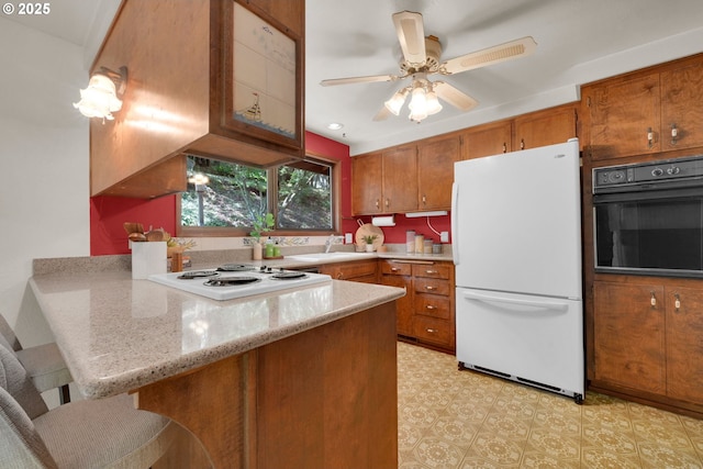 1770 W 28th Ave, Eugene, OR 97405 - kitchen featuring white appliances, a peninsula, brown cabinetry, a breakfast bar area, and a ceiling fan