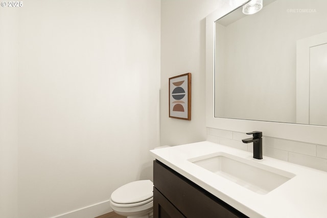 half bathroom featuring decorative backsplash, toilet, vanity, and baseboards