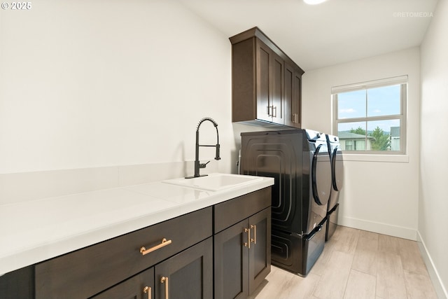 laundry area with light wood-style flooring, washer and clothes dryer, a sink, cabinet space, and baseboards