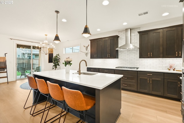 kitchen with visible vents, stainless steel gas cooktop, a sink, wall chimney exhaust hood, and tasteful backsplash