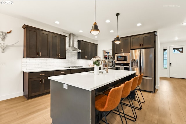 kitchen featuring tasteful backsplash, wall chimney range hood, light wood-style floors, stainless steel appliances, and a sink