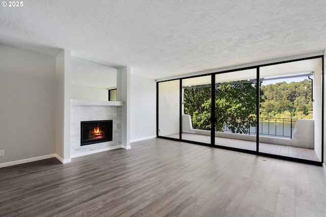 unfurnished living room with a wall of windows, wood finished floors, a textured ceiling, a warm lit fireplace, and baseboards