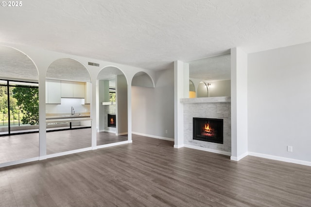 unfurnished living room featuring a warm lit fireplace, dark wood-style flooring, a sink, baseboards, and a textured ceiling