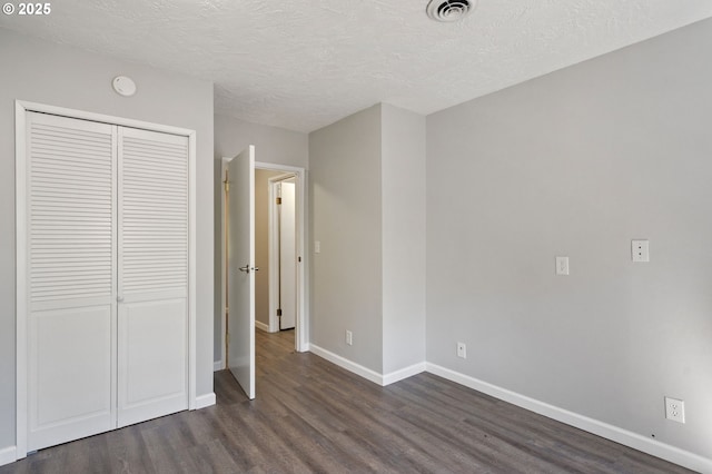unfurnished bedroom featuring dark wood-style flooring, a closet, baseboards, and a textured ceiling