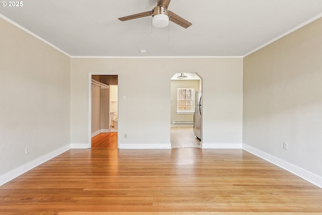 spare room featuring light hardwood / wood-style floors, baseboard heating, crown molding, and ceiling fan