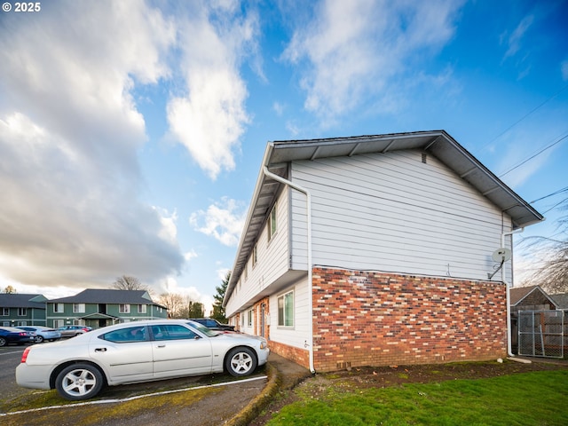 view of side of home featuring a yard, uncovered parking, and brick siding