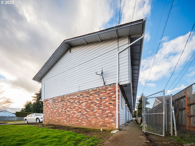 view of property exterior with brick siding, a lawn, and fence