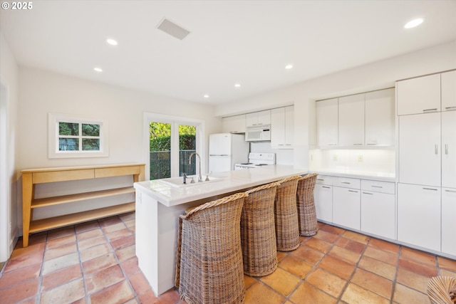 kitchen featuring white appliances, white cabinetry, decorative backsplash, sink, and a breakfast bar area