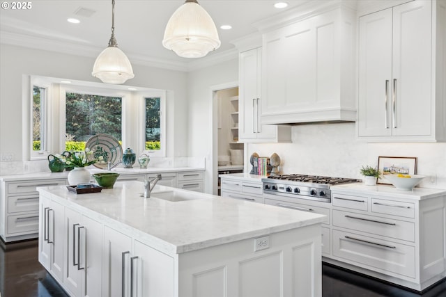 kitchen with light stone countertops, white cabinets, an island with sink, hanging light fixtures, and stainless steel gas stovetop