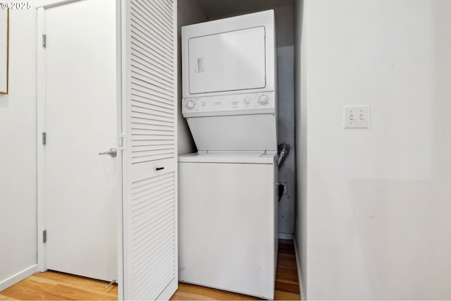 laundry room with stacked washing maching and dryer and light hardwood / wood-style flooring