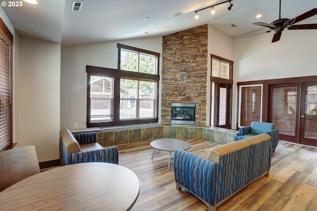 living room featuring hardwood / wood-style floors, a stone fireplace, high vaulted ceiling, and ceiling fan