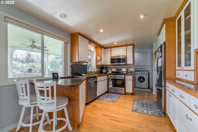 kitchen with appliances with stainless steel finishes, a breakfast bar, sink, dark stone countertops, and washer / dryer
