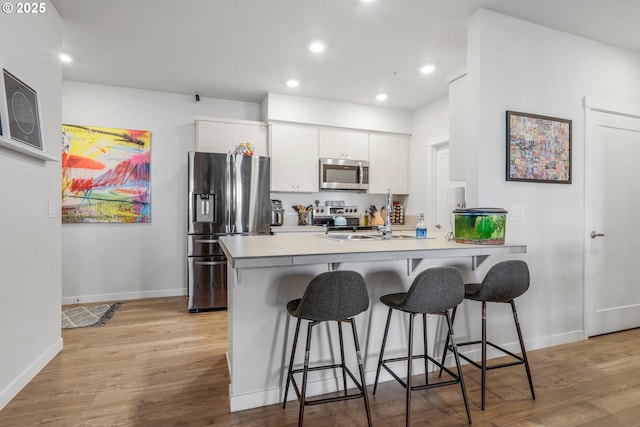 kitchen with appliances with stainless steel finishes, a kitchen bar, white cabinetry, light hardwood / wood-style floors, and sink