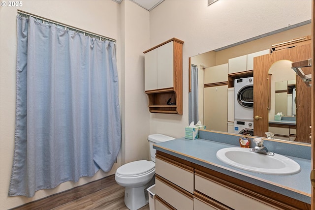 full bathroom featuring wood-type flooring, stacked washer and dryer, vanity, toilet, and shower / bath combo