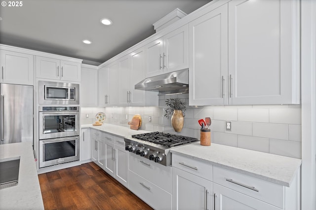 kitchen with dark wood-style flooring, backsplash, white cabinetry, built in appliances, and under cabinet range hood