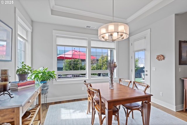 dining space featuring a chandelier, wood finished floors, visible vents, baseboards, and a tray ceiling