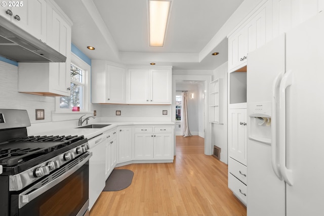 kitchen featuring white appliances, a raised ceiling, under cabinet range hood, white cabinetry, and a sink