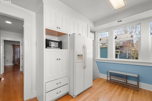 kitchen with light wood-style flooring, white cabinetry, baseboards, white fridge with ice dispenser, and stainless steel microwave