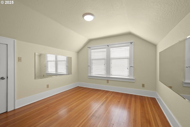 additional living space with wood-type flooring, baseboards, vaulted ceiling, and a textured ceiling