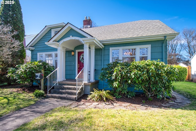 bungalow-style home with a shingled roof, a chimney, and a front yard