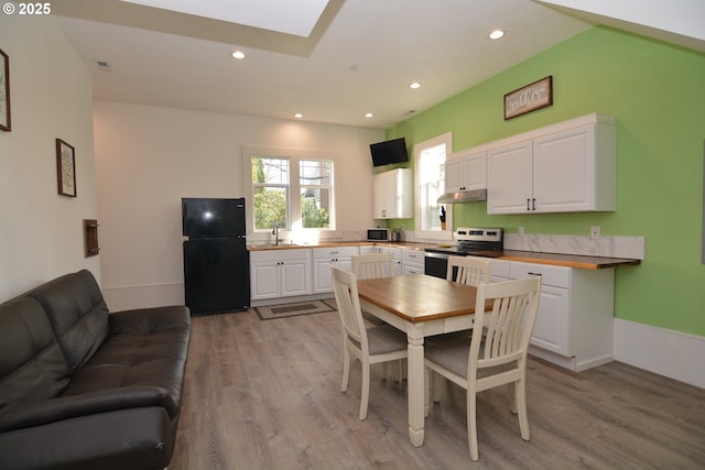 kitchen featuring light wood finished floors, white cabinets, freestanding refrigerator, under cabinet range hood, and stainless steel range with electric stovetop