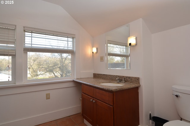 bathroom with lofted ceiling, a healthy amount of sunlight, toilet, and vanity